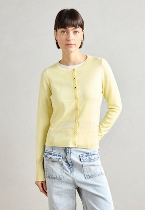 Lys gul strikket cardigan med rund hals, knappelukking foran og lange ermer. Matcher med høyhalsede denimjeans.