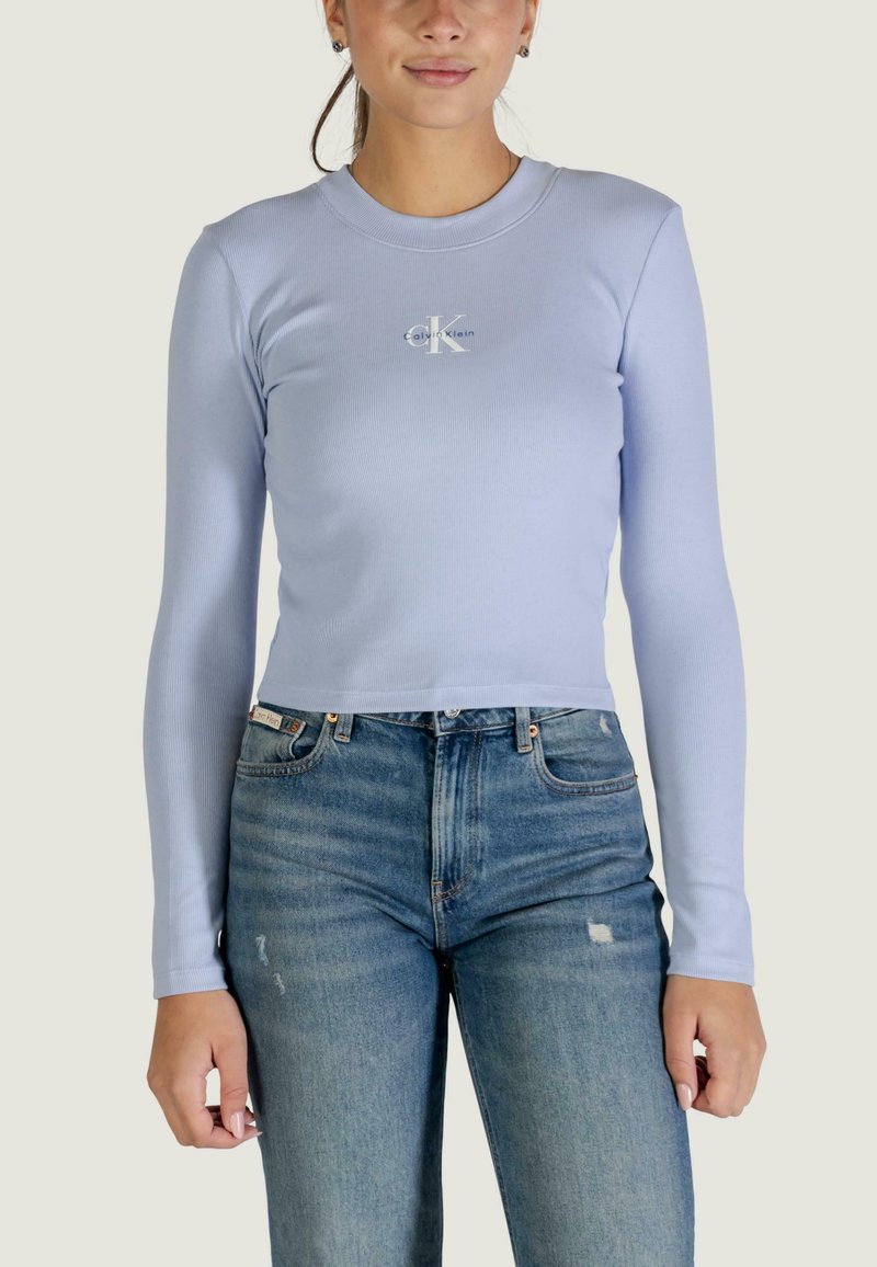 Top corto a maniche lunghe azzurro chiaro in tessuto a costine, con piccolo logo bianco al centro davanti, abbinato a jeans di denim a vita alta.