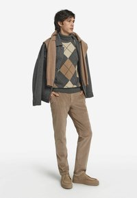 Grau-wollener Mantel über einem creme- und braunfarbigen Argyle-Pullover, beigen Cordhosen und braunen Schuhen. Lässige Passform mit strukturierten Stoffen und lässigen Lagen.