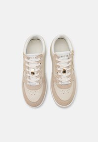 Baskets beige avec une tige en cuir lisse agrémentée d'accents en suède, des lacets plats blancs, des détails en métal doré et des perforations sur la boîte à orteils.