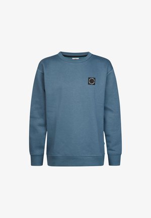 Niebieska bluza z okrągłym dekoltem, długimi rękawami i małą czarną okrągłą naszywką z logo na lewym torsie.