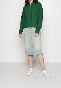 Zelený svetr s krátkým zipem a límcem, zkombinovaný s světle modrou denimovou midi sukní a bílými platformovými teniskami. Jednoduchý design, uvolněný střih.