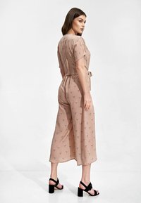 Różowy kombinezon z wcięciem w talii, krótkimi rękawami i wzorami ptaków; zestawiony z czarnymi sandałami na słupku.