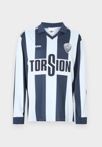 Ποδοσφαιρική φανέλα με μακριά μανίκια, με κάθετες ρίγες σε ανοιχτό και σκούρο μπλε, γιακά και γράμματα «TORSION» με έντονη μαύρη γραμματοσειρά.
