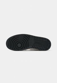 Semelle en caoutchouc noire d'une basket Nike avec des motifs circulaires et rectangulaires, montrant le logo Nike au centre.