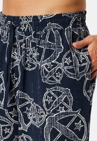 Shorts de pyjama bleu marine avec un motif abstrait blanc incluant des étoiles et des designs circulaires. Taille élastique avec cordon de serrage et poches latérales.