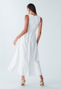 Balta maxi suknelė su aptempta tekstūruota liemenėle ir laisvai krentančia sijono dalimi. Yra apvalus nugaros iškirpimas ir subtilios klostės. Derinama su aukštakulniais sandalais.
