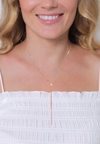 Náhrdelník z ružového zlata v prekr�ývajúcom sa dizajne s jemným, predĺženým kvapkovým tvarom, ktorý má okrúhly akcent a hladký, lesklý povrch.