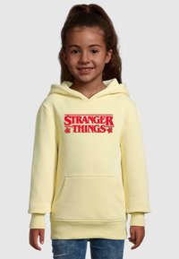Gul luvtröja med ficka fram och röd "STRANGER THINGS" grafik. Har ribbade muddar och nederkant, mjukt material.