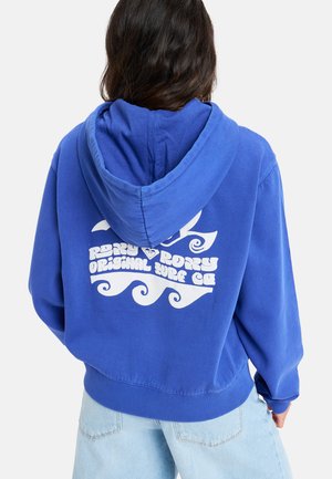 Blå hoodie med en framficka, med en vit grafisk logotypdesign på baksidan. Mjukt tyg med ribbade ärmslut och nederkant.