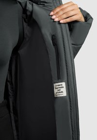 Grå pufferjakke indvendig med glat tekstur, med en lynlås lomme og et stofmærke, der står "Et varmt kram lavet af stof."