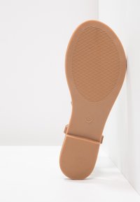 Tan rubberi sandaalien pohja, jossa on uurrettu pinta, avonainen varvasmuotoilu ja nilkkahihna. Koko merkitty kantapäähän numero 37.