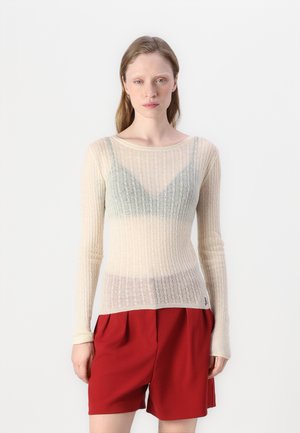 Haut long à manches avec un motif en côtes beige clair, doté d'une texture transparente, avec un détail de superposition triangulaire bleu clair au niveau de la poitrine. Short rouge.
