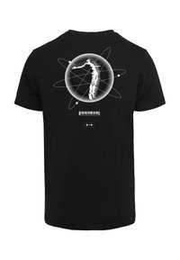 Zwart katoenen T-shirt met een afbeelding van een figuur binnen een cirkelvormig ontwerp dat op een atoom lijkt. Voorzien van een streepjescode en tekst onder de afbeelding.