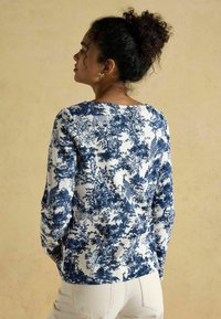 Sinine ja valge muster pikkade varrukatega pluus, millel on lilleline disain koos loomadega, pehme puuvillane kangas, ümar kaelus ja lõdvestunud lõige.