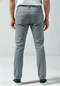 Grijze slim-fit broek met een gladde textuur en achterzakken, gecombineerd met zwarte sneakers. Zichtbare stiksels en een gestroomlijnd ontwerp.