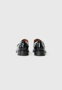 Scarpe di pelle nera con una finitura lucida, punta arrotondata e una suola nera bassa. Presentano una texture liscia e un design minimalista.