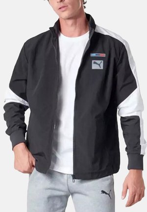 Veste bomber noire avec des accents blancs, fermeture éclair, col montant et patch logo. Fabriquée en matériau lisse, elle possède des manches longues.