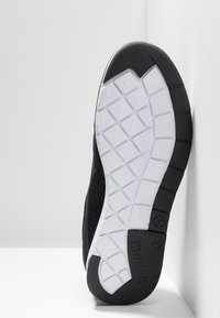 Black athletic shoe with a flexible rubber sole featuring a textured white outsole, designed for traction and comfort, angled against a white background.