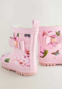 Bottes de pluie pour tout-petits roses avec des motifs floraux et de papillons, intérieur doublé, et des nœuds décoratifs avec des accents en or rose sur les côtés.