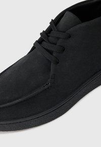 Chaussure noire en daim à lacets avec un design à profil bas, surface texturée et couture subtile. Présente une semelle en caoutchouc pour une meilleure adhérence.