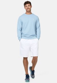 Sudadera azul claro con puños y dobladillo acanalados, combinada con pantalones cortos blancos. El conjunto se completa con zapatillas de running grises y azules.