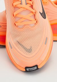 Nahaufnahme von orangen Nike-Laufschuhen mit Mesh-Struktur, Schnürsenkeln, schwarzen Swoosh-Logos und gepolsterter Sohle auf weißem Hintergrund.