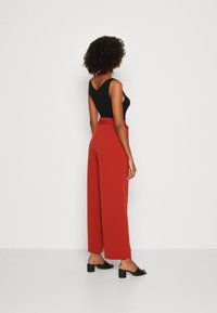 Haut sans manches noir associé à un pantalon large rouge taille haute. La tenue présente un nœud à la taille et des sandales à talons blocs noires.