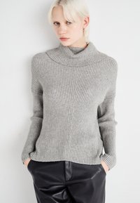 Pull en maille côtelée gris clair avec un col montant, des manches longues et une coupe décontractée, associé à un pantalon en cuir noir. Design minimaliste texturé.