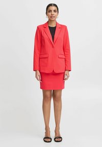 Koraalblazer met twee voorzakken en een enkele knoopsluiting, gecombineerd met een bijpassende pencil skirt. Glad stof en aansluitende pasvorm.