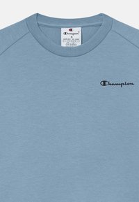 T-shirt bleu clair à col rond avec le logo Champion noir sur la poitrine gauche et une étiquette de taille indiquant petit et âge 7/8 ans.