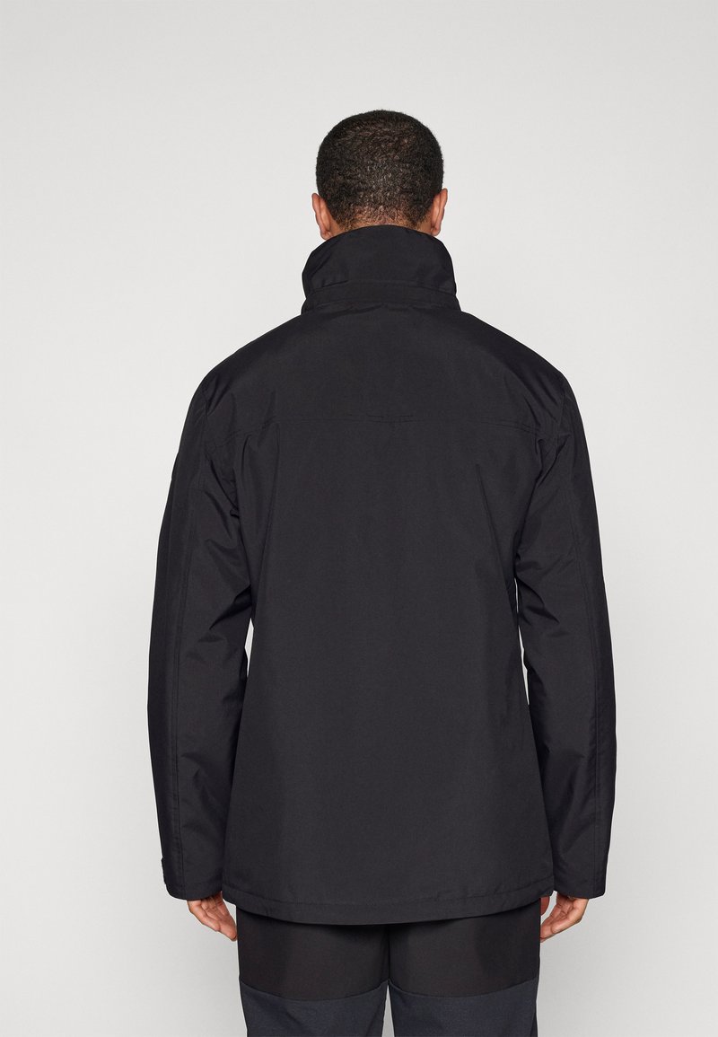 Schwarze Jacke mit hohem Kragen, aus glattem Stoff gefertigt. Hat eine lässige Passform und Steppnähte. Rückansicht, kombiniert mit dunklen Hosen.