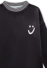 Black fleece sweatshirt with a ribbed striped collar. Features a white smiley face embroidered on the left chest. Soft texture and relaxed fit.