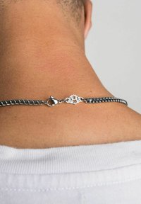 Colier din argint cu un închizător în formă de floare de lotus, având un finisaj neted și strălucitor pe pielea dezgolită, purtat la gât.