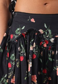 Gros plan d'une jupe noire fleurie avec des roses rouges et roses, tissu froncé et détail de lien sur le côté près d'un ventre nu.