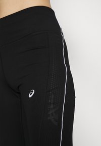 Schwarze Sportleggins mit hohem Bund, ausgestattet mit weißen Seitenstreifen und strukturierten Akzenten in verschiedenen Schwarznuancen.