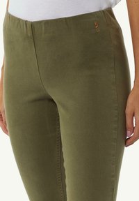 Olijfgroene stretchbroek met een gladde textuur en een elastische tailleband. Heeft een klein logo-accent nabij de tailleband.
