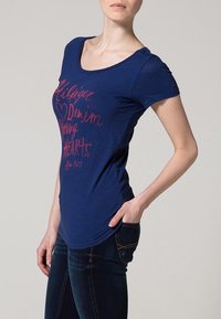 Mörkblå t-shirt med rund halsringning, korta ärmar och röd grafisk text. Mjuk, lätt tygkvalitet med en avslappnad passform.