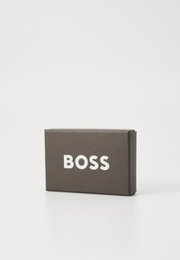 Scatola rettangolare grigia scura con una texture liscia che presenta la parola "BOSS" in lettere bianche in grassetto sulla parte anteriore.