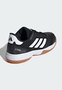 Chaussure de sport noire avec des accents blancs, dotée d'une tige en synthétique, d'une semelle en caoutchouc et de panneaux texturés. "LIGRA" embossé sur le talon.