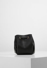 Černá kožená kabela ve tvaru kýble se zlatými detaily, měkkou texturou a šňůrkovým uzávěrem, s zaoblenými okraji a minimalistickým designem.