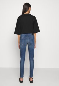 Black oversized t-shirt with a round neck worn with slim-fitting blue denim jeans. The jeans feature a mid-rise waist and back pockets.