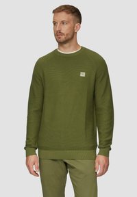 Pull vert foncé en tricot texturé, avec un col rond, des poignets côtelés et un petit patch de marque sur la poitrine.