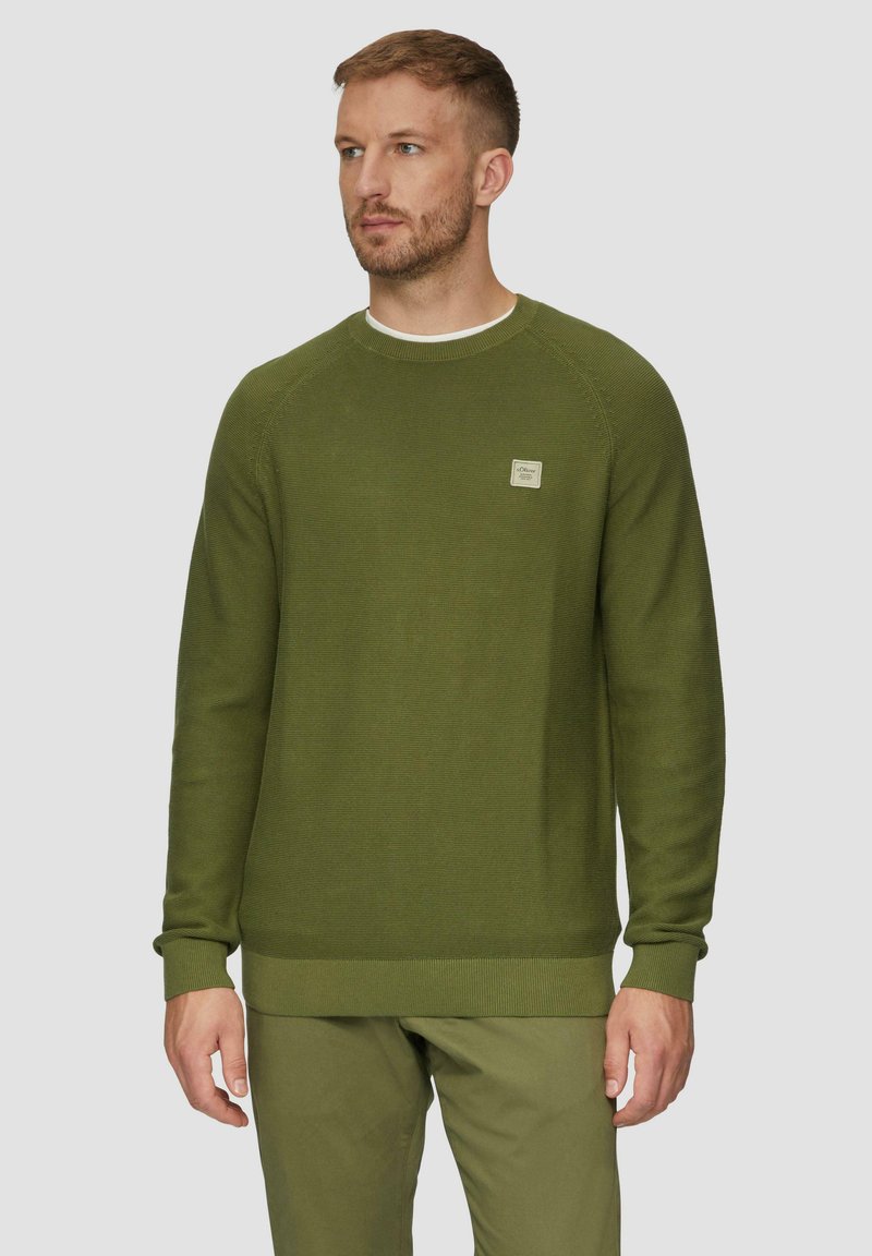 Pull vert foncé en tricot texturé, avec un col rond, des poignets côtelés et un petit patch de marque sur la poitrine.