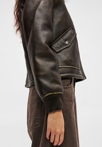 Crna kožna jakna s oblikovanim dizajnom, rebrastim manžetama, s džepom na zakopčavanje i kontrastnim žutim šavovima.