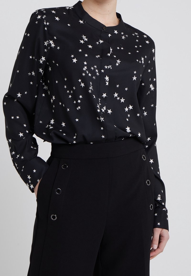 Svart blus gjord av glatt tyg med ett stjärnmönster i vitt. Har en rund halsringning och långa ärmar. Matchad med högmidjade svarta byxor.