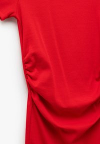 Top in tessuto a coste rosse con maniche corte e dettaglio arricciato sui lati per un aspetto testurizzato. Finitura liscia con una leggera lucentezza.
