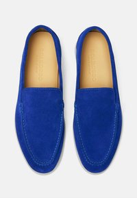 Plave nubuk slip-on cipele s zaobljenim nosom, kontrastnim šavovima i kožnom unutrašnjošću na bijeloj potplati. Pogodne za ležerno nošenje.