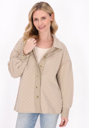 Beige prošívaná bunda s límečkem, velkými knoflíky a uvolněným střihem, zkombinovaná s lehkým topem a džíny.