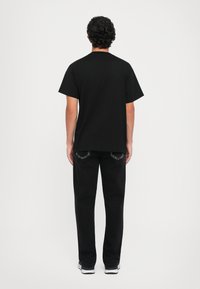 Svart t-skjorte med korte ermer kombinert med svarte bukser. T-skjorten har en rett fasong; buksene har standard passform med baklommer.